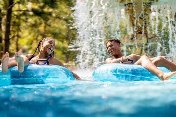 Boy and girl on innertubes going under water fall