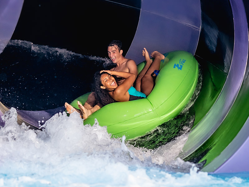 Teenagers in tube on waterslide, laughing.