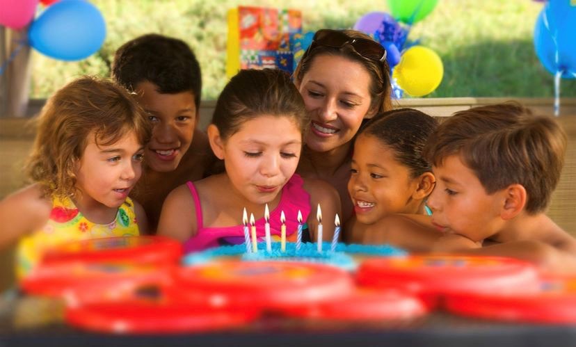 Children around a birthday cake, blowing out the candles