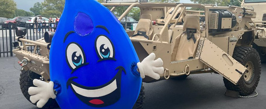 Blue drop mascot in front of military truck